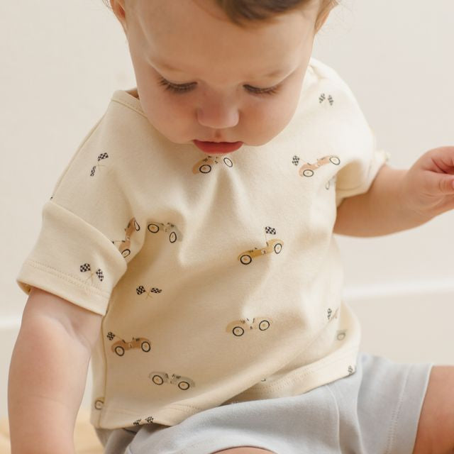 Child wearing a cream-colored shirt with car patterns on a neutral background