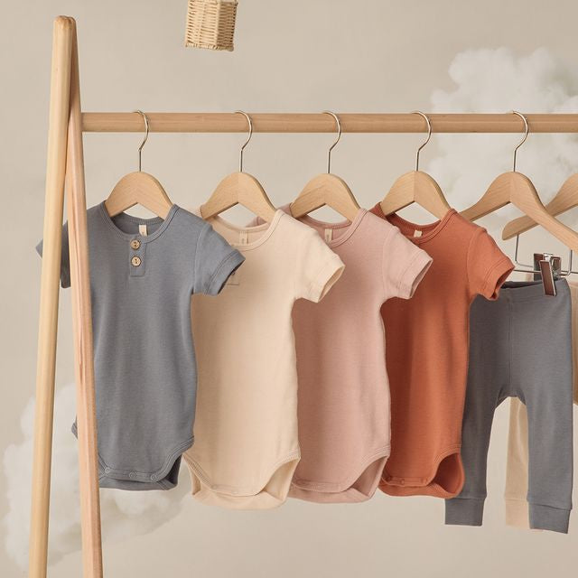 Wooden clothing rack with baby clothes on a neutral background
