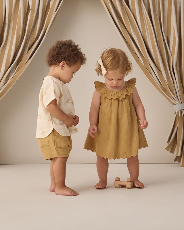 Two children, a boy and a girl, standing in front of striped curtains.