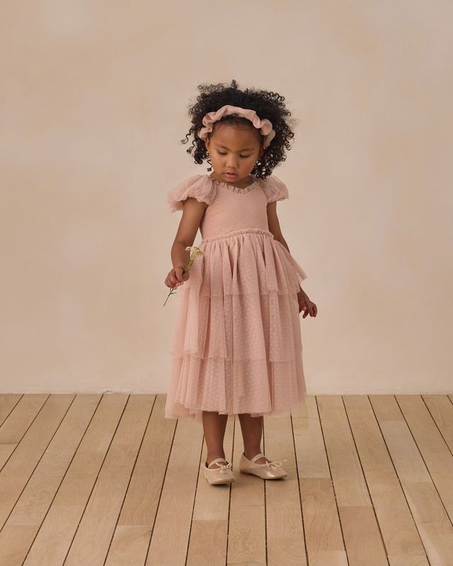 Young girl in a pink dress standing on a wooden floor with a plain background