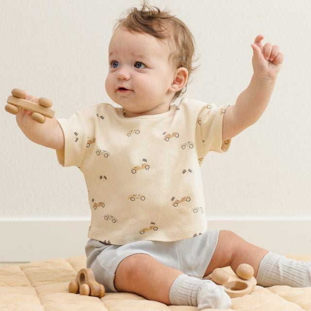 Baby wearing a cream-colored shirt with small patterns, sitting on a beige blanket.