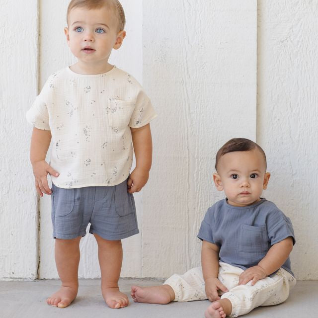 Two young children wearing matching outfits against a white wooden background
