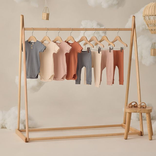 Wooden clothing rack with baby clothes on a neutral background
