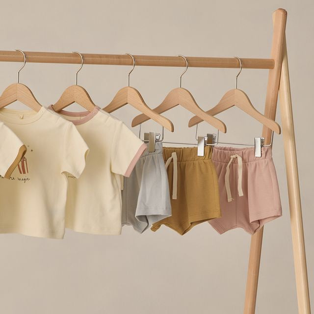 Children's clothing on hangers against a beige wall