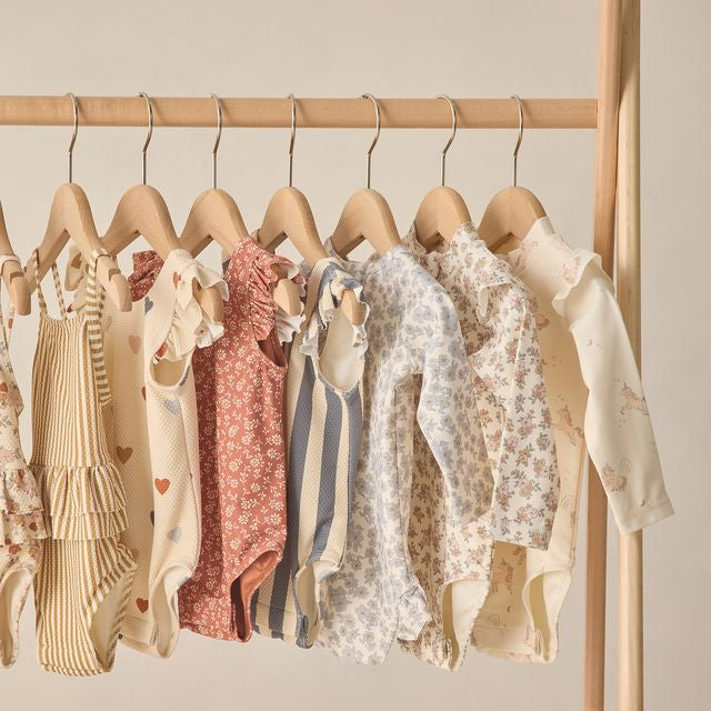 Collection of baby clothes on hangers against a beige wall
