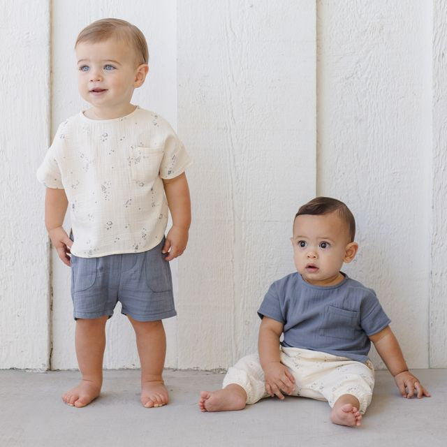 Two toddlers wearing matching outfits against a white wall.