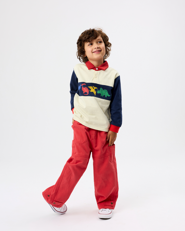 A young boy modeling a color-blocked long-sleeve polo shirt with red pants, standing against a plain white studio background.