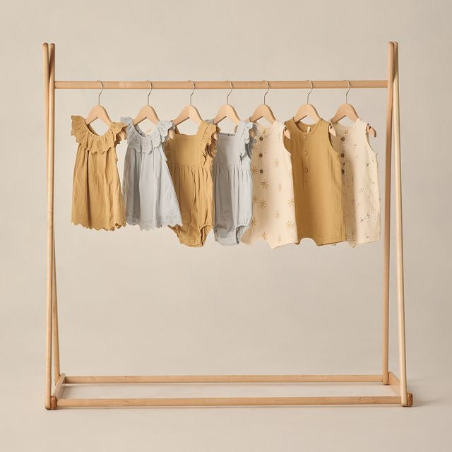 Children's dresses hanging on a wooden rack against a beige background