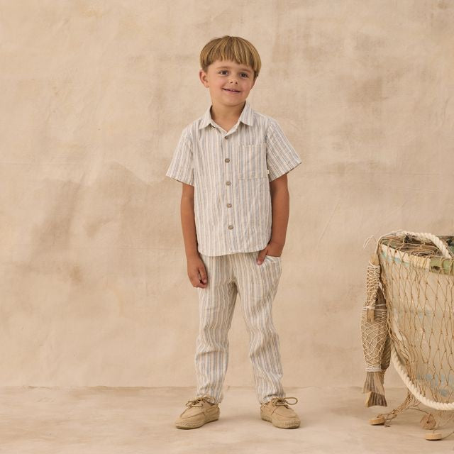 Young boy in striped shirt and pants standing next to a wicker basket against a beige background