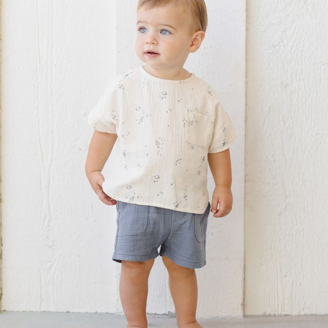 Child wearing a white shirt with small patterns and gray shorts against a white background