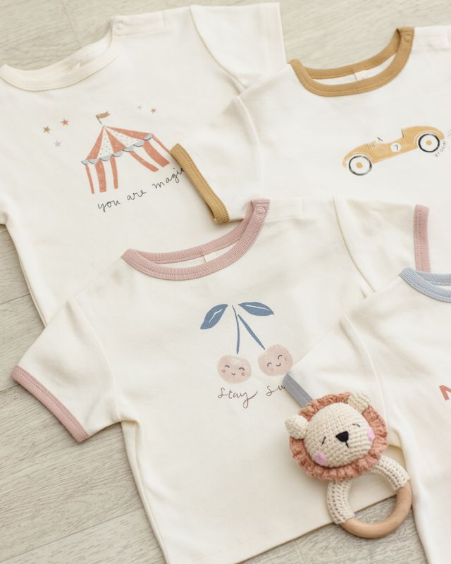 Baby outfit with t-shirt and lion rattle on a light wooden surface