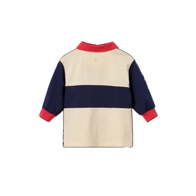 A long-sleeve colorblock rugby-style shirt shown from the back, featuring a cream body, a navy blue horizontal stripe, and red trim on the collar and cuffs.