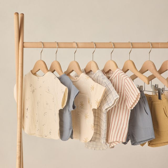 Children's clothing on wooden hangers against a beige wall