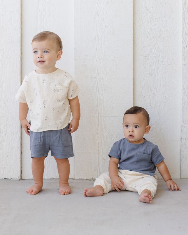 Two toddlers wearing matching outfits against a white wall.