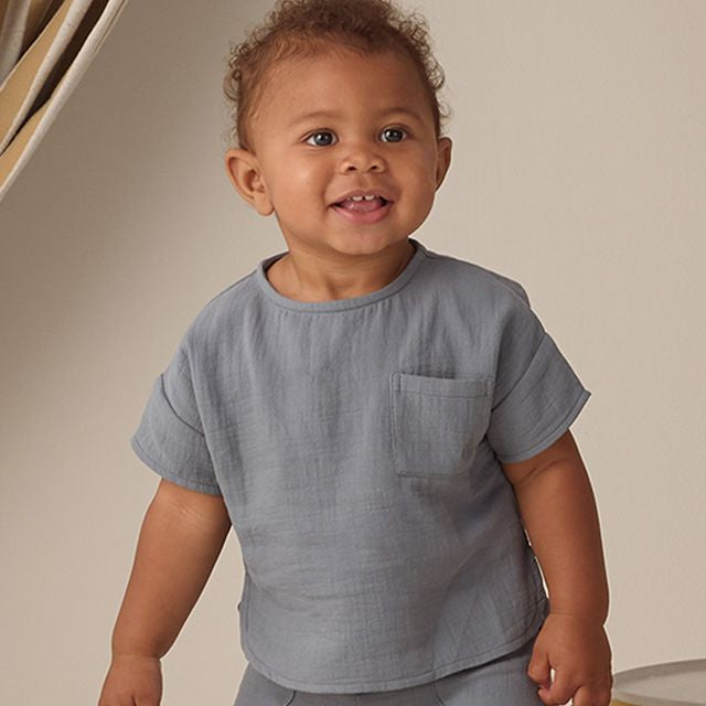 Child wearing a gray outfit standing against a neutral background