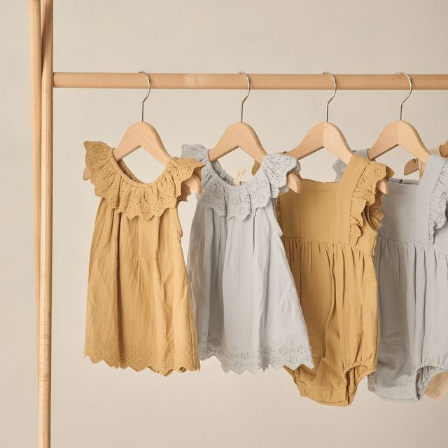 Four children's dresses in yellow and gray on hangers against a beige background