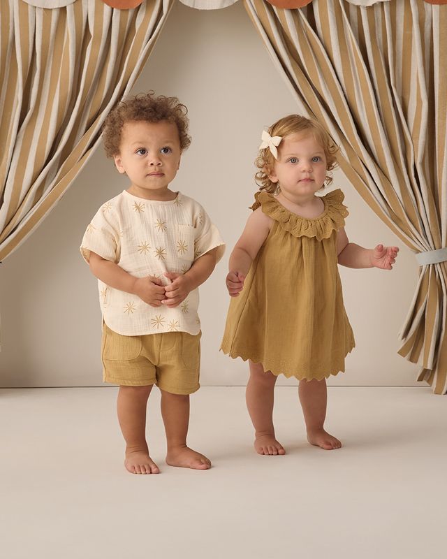 Two children, a boy and a girl, standing in front of striped curtains.