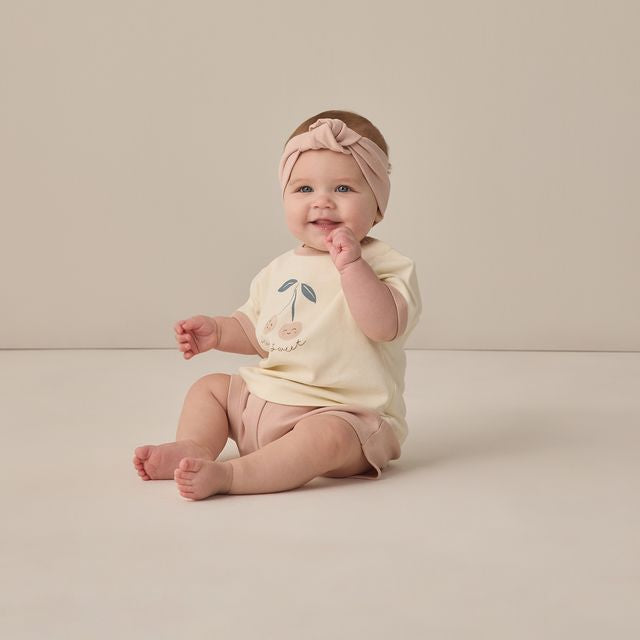 Baby sitting on a plain background wearing a light-colored outfit with a floral design.