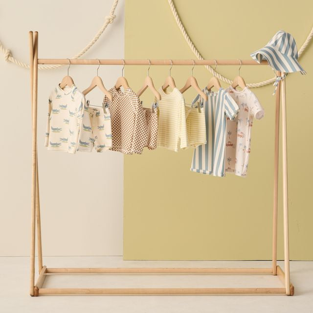 Children's clothing on a wooden rack against a light green wall.
