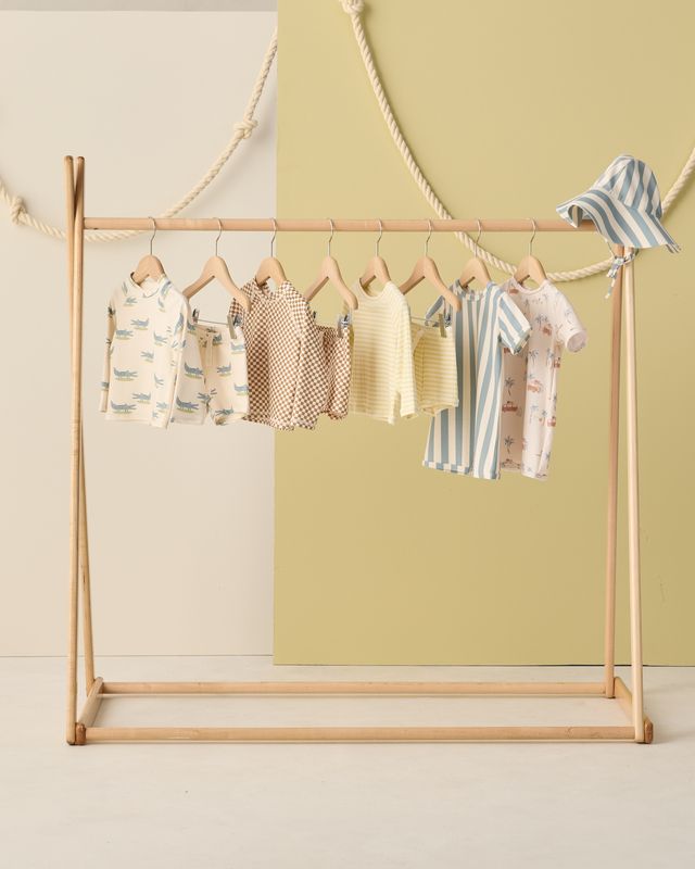 Children's clothing on a wooden rack against a light green wall.