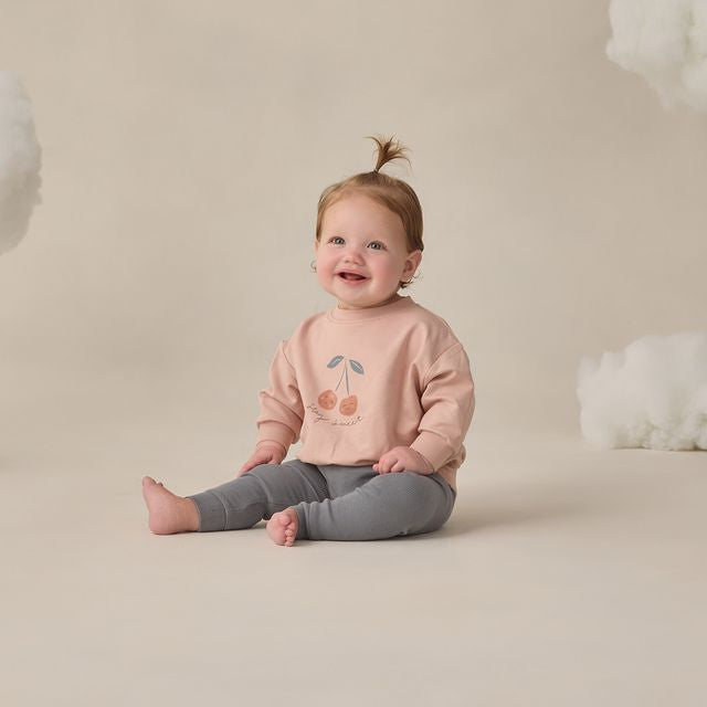 Child wearing a pink sweater with a cherry design on a beige background