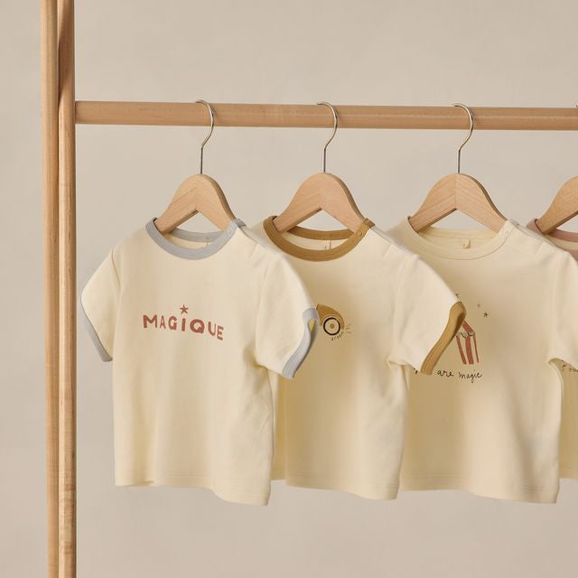 Three children's t-shirts on hangers against a beige wall.