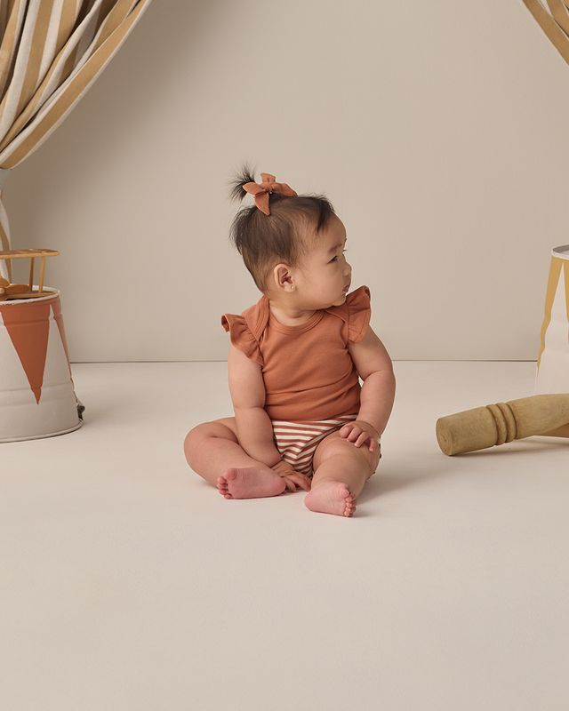 Baby sitting on a light-colored floor with a neutral background
