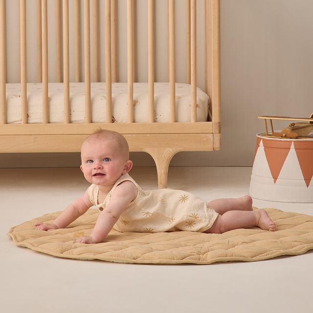 Baby crawling on a beige mat in front of a wooden crib with a neutral background