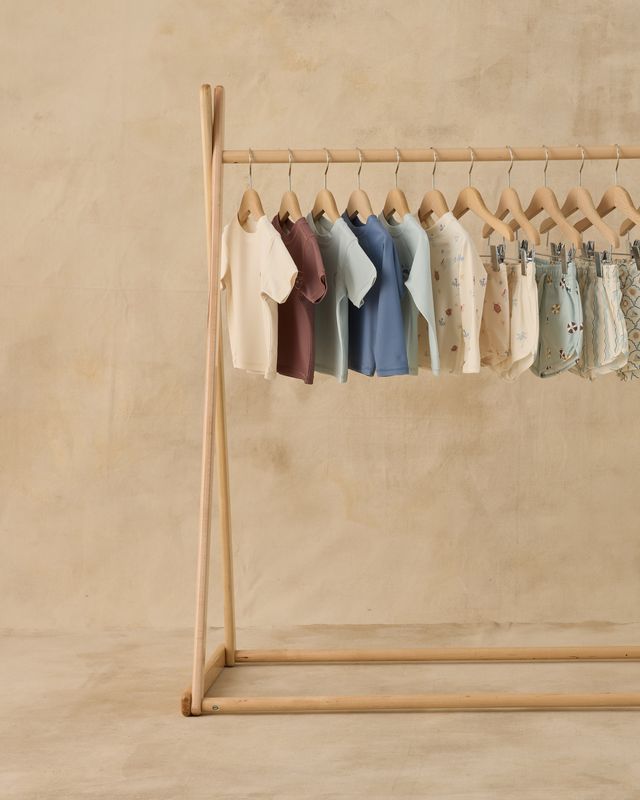 Wooden clothing rack with baby clothes on a beige background
