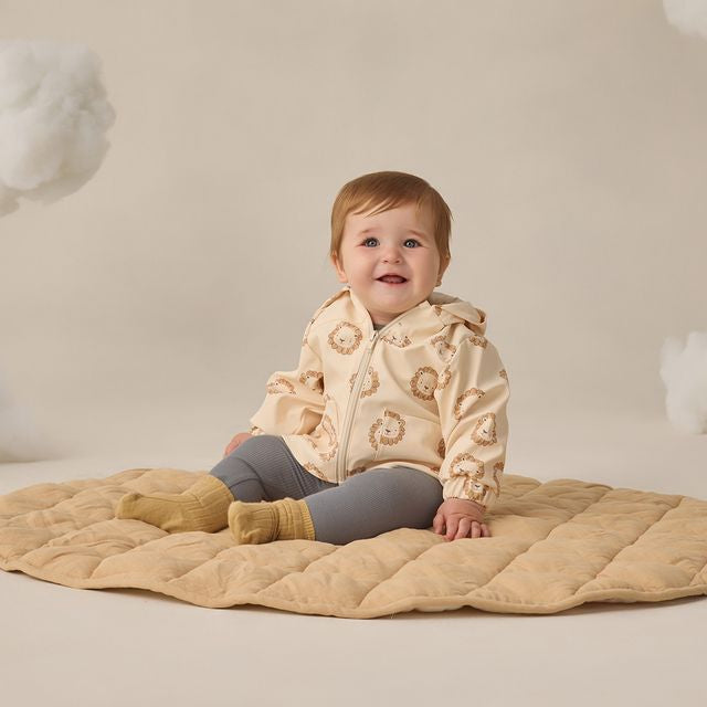 Baby wearing a beige quilted jacket sitting on a beige blanket with a neutral background