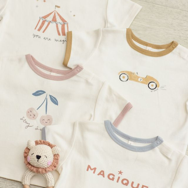 Two baby onesies with cartoon designs and a lion rattle on a textured surface.