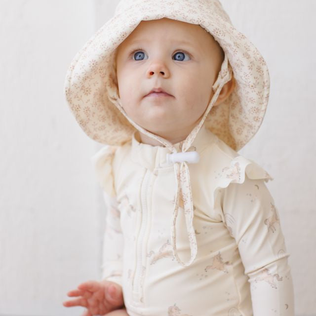 Baby wearing a cream-colored hooded outfit with a plain background