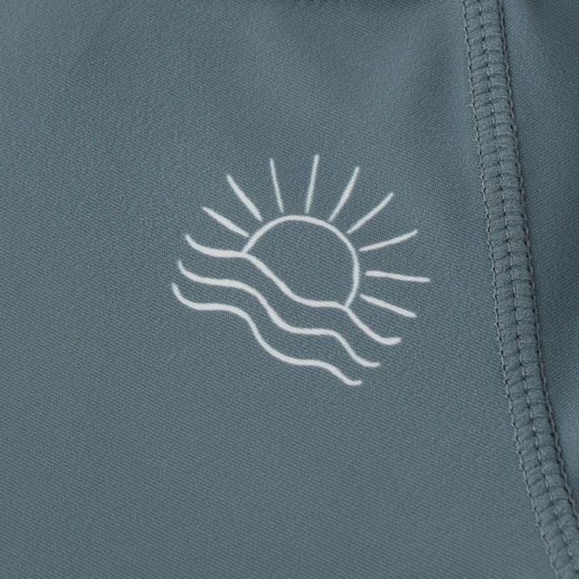 Close-up of a blue garment with a white sun and wave design on a matching background.
