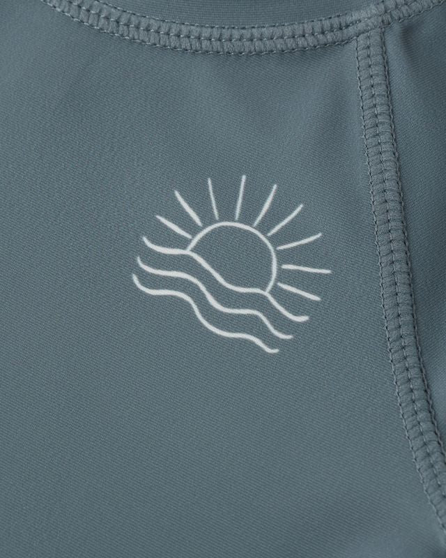 Close-up of a blue garment with a white sun and wave design on a matching background.