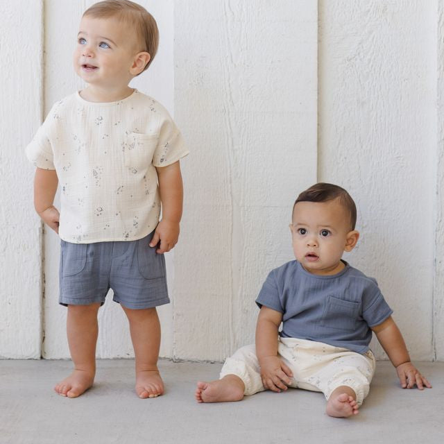Two young children wearing casual clothing against a white wooden panel background