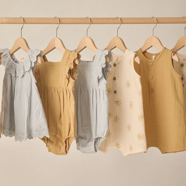 Children's clothing including dresses and rompers on hangers against a neutral background
