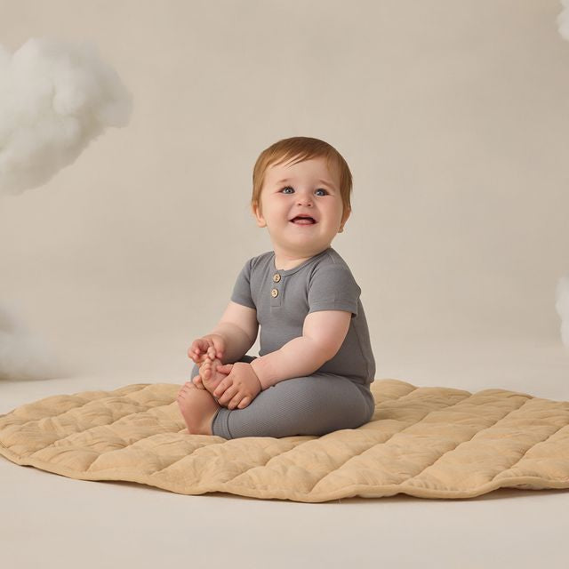 Baby sitting on a beige blanket against a neutral background