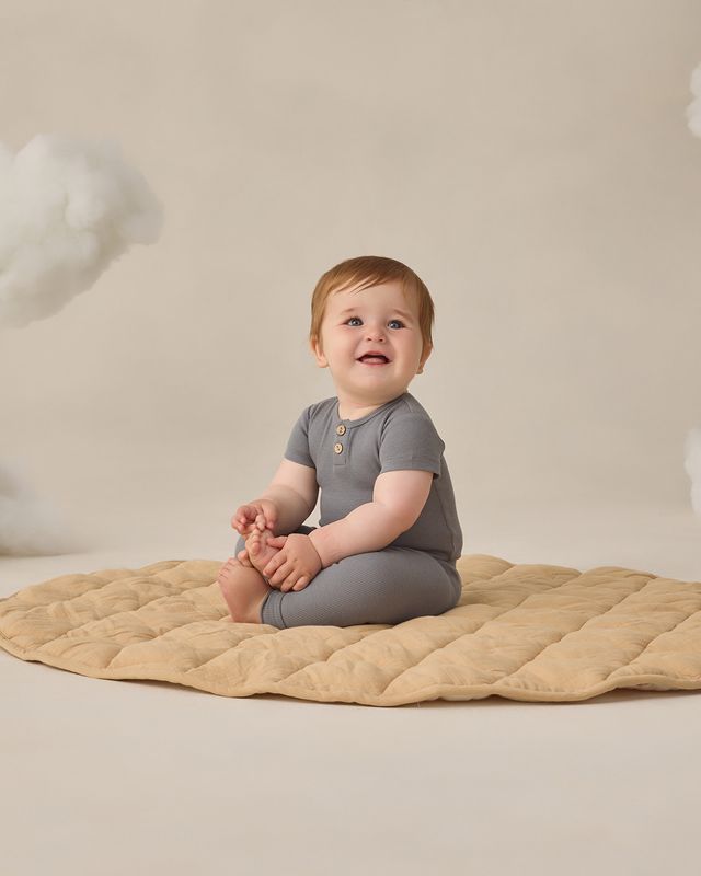 Baby sitting on a beige blanket against a neutral background