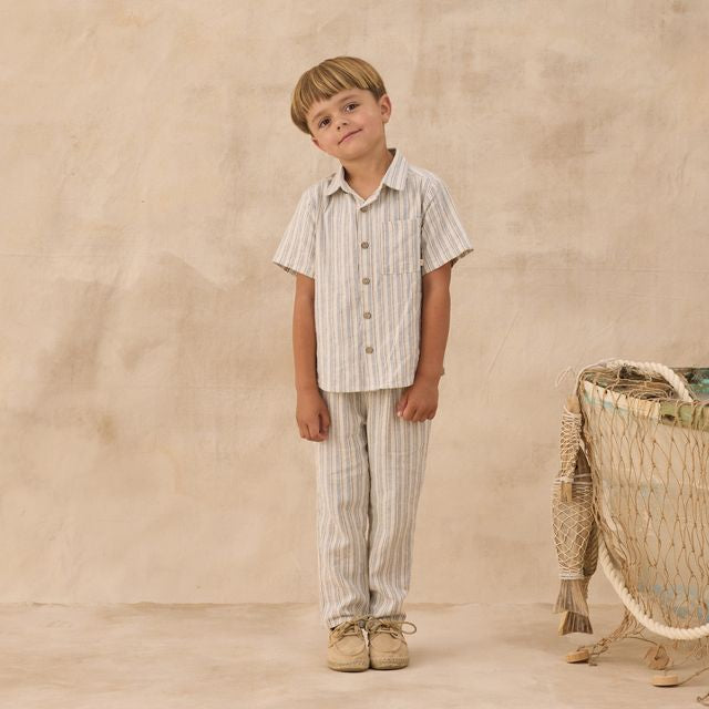 Young boy in striped shirt and pants standing next to a woven basket on a beige background
