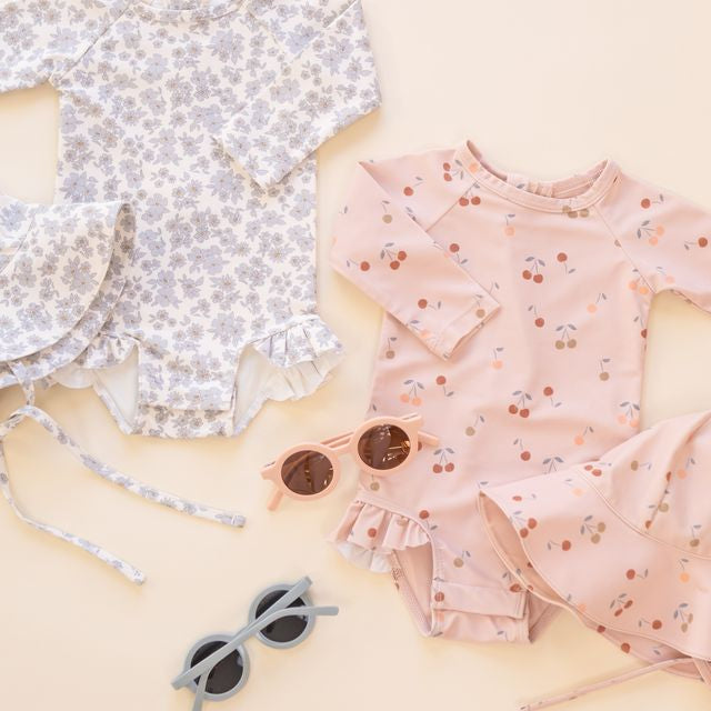 Children's floral dress and swimsuit with sunglasses on a light background