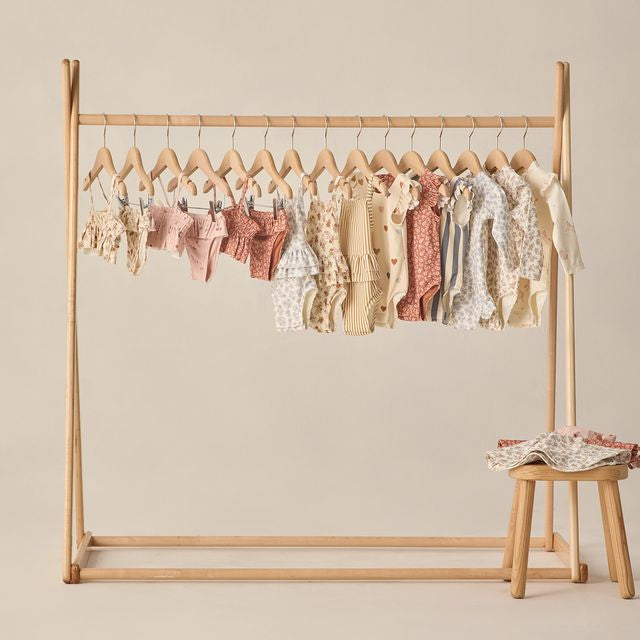 Wooden clothing rack with baby clothes on a beige background