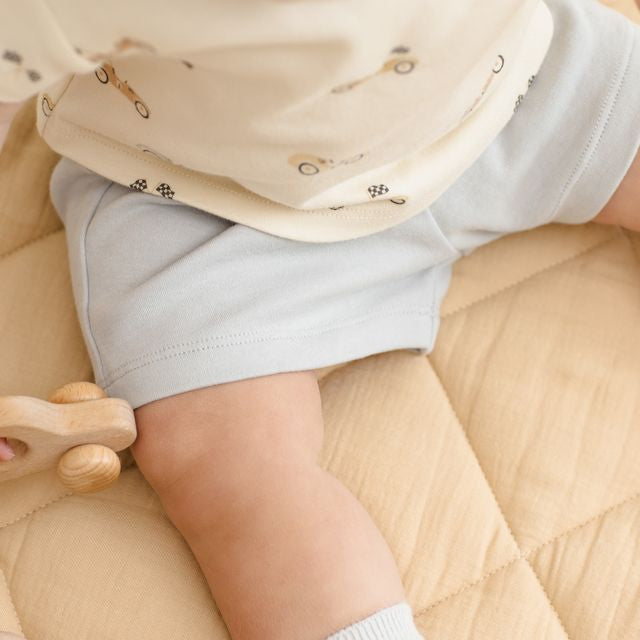 Close-up of a baby wearing a light-colored bib and shorts, sitting on a beige surface.