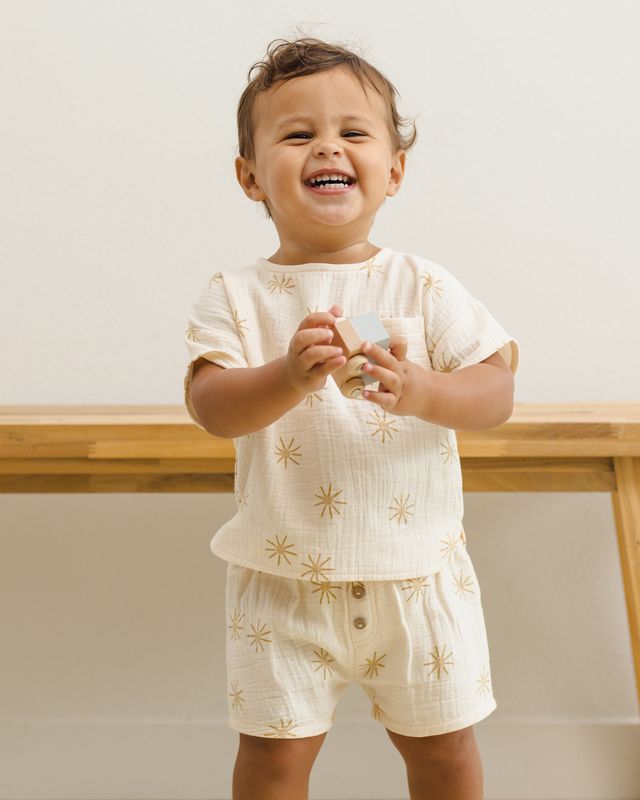 Child wearing a cream-colored outfit with star patterns, standing indoors.