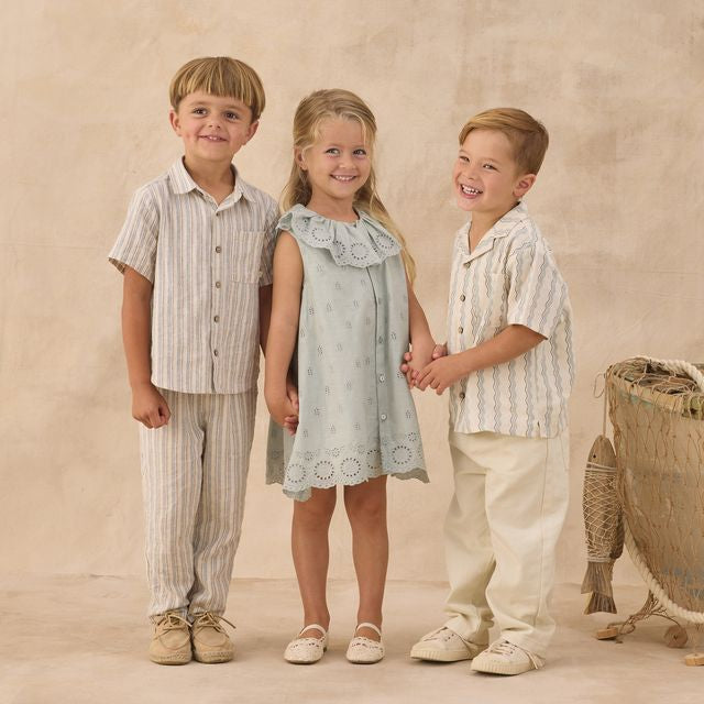 Three children standing together in a studio setting with a beige background