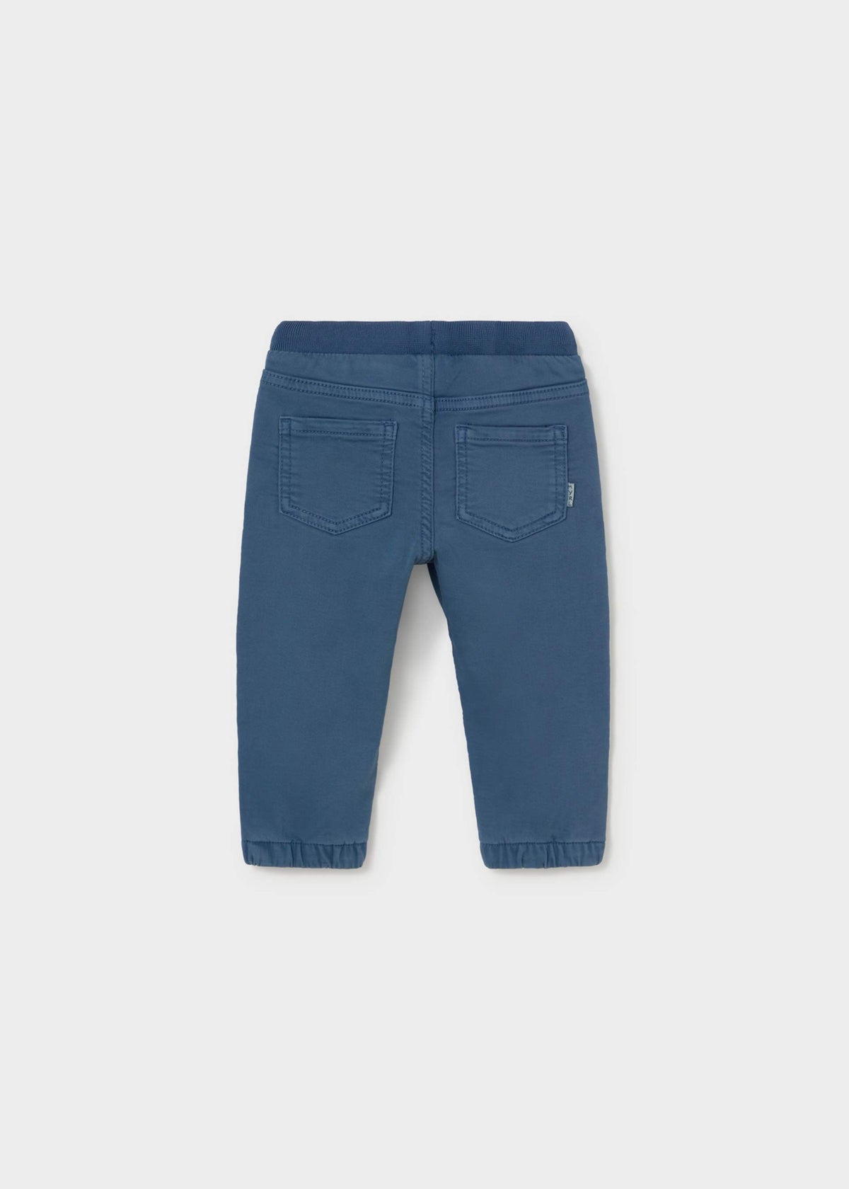 Blue denim pants shown from the back, featuring a wide elastic waistband, two back patch pockets, and elastic cuffs at the ankles, photographed on a light gray background.