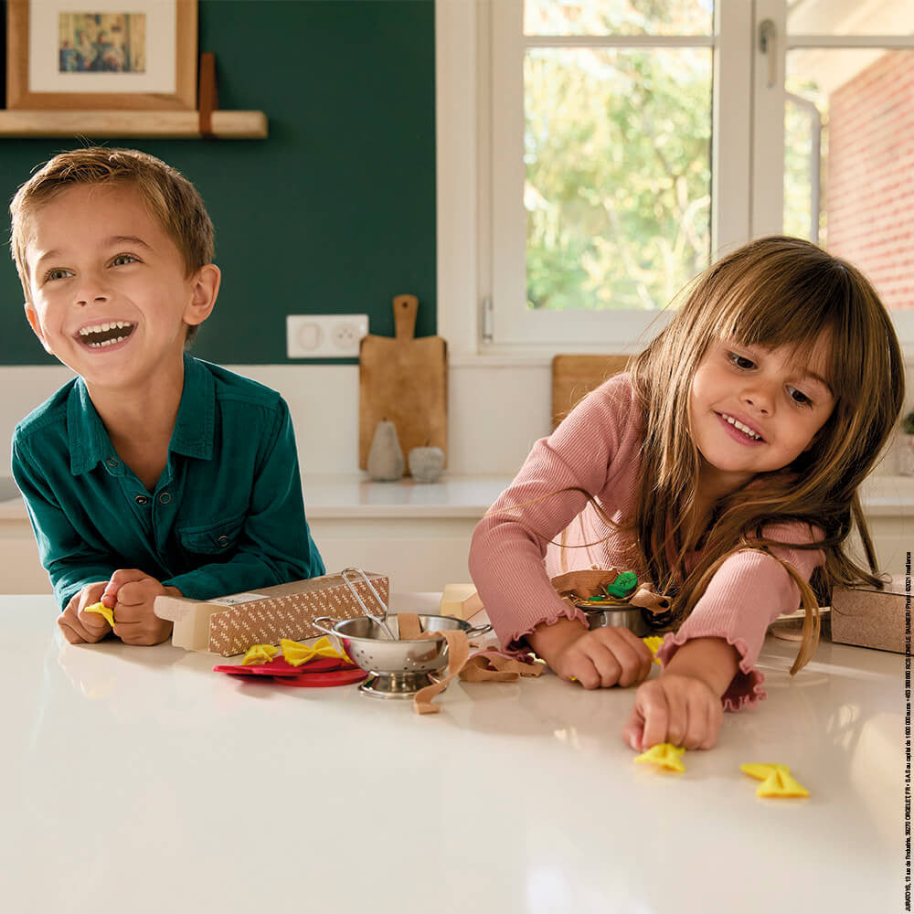 Two children playing with play dough on a kitchen counter.