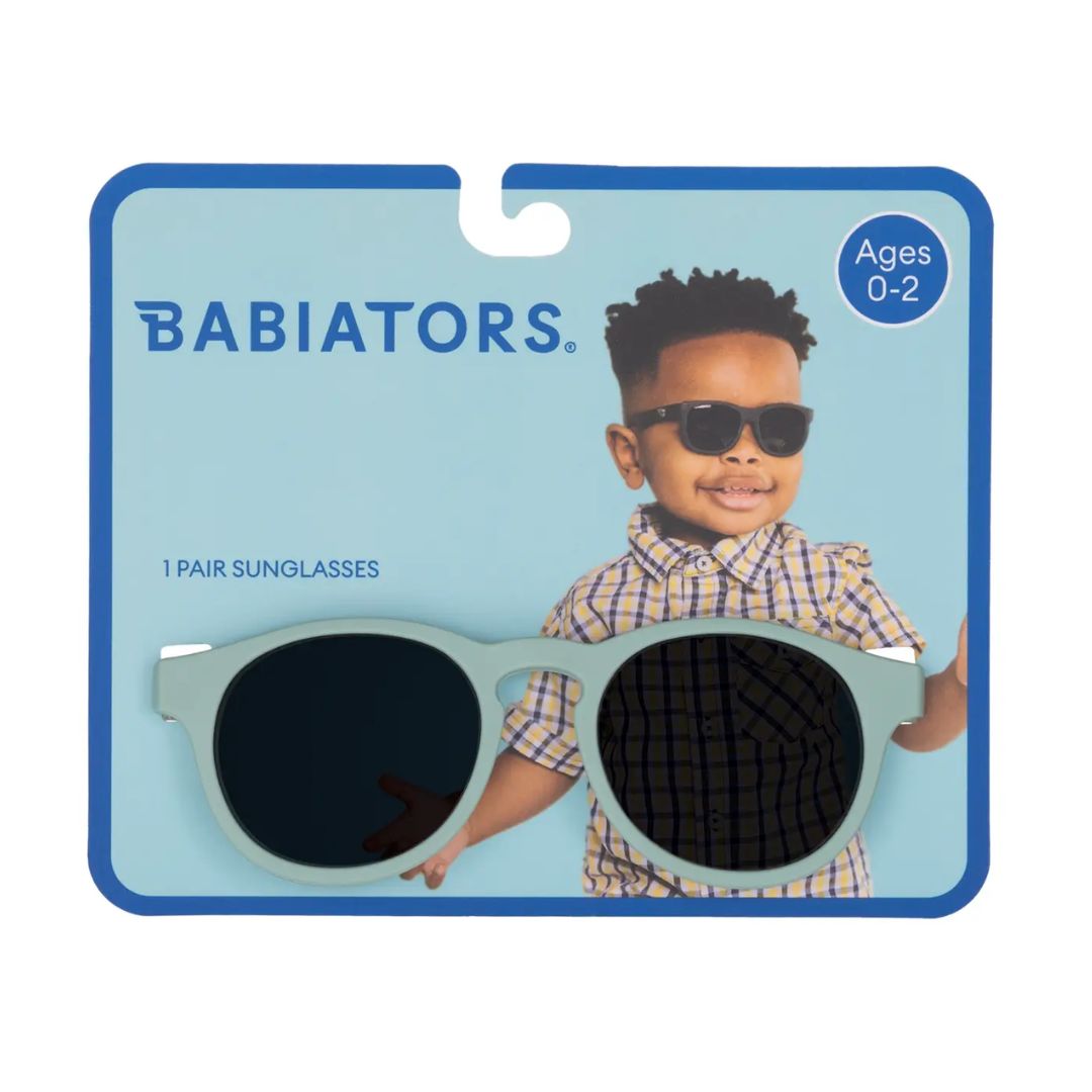 Babiators brand children's sunglasses in a light mint green color, presented on their original blue and white cardboard retail packaging. The packaging features the Babiators logo, an age rating of 0-2, and a photo of a young boy wearing the sunglasses.