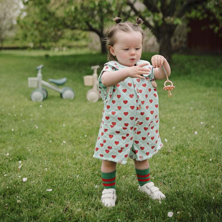 Child in a heart-patterned outfit playing with a toy in a grassy area.