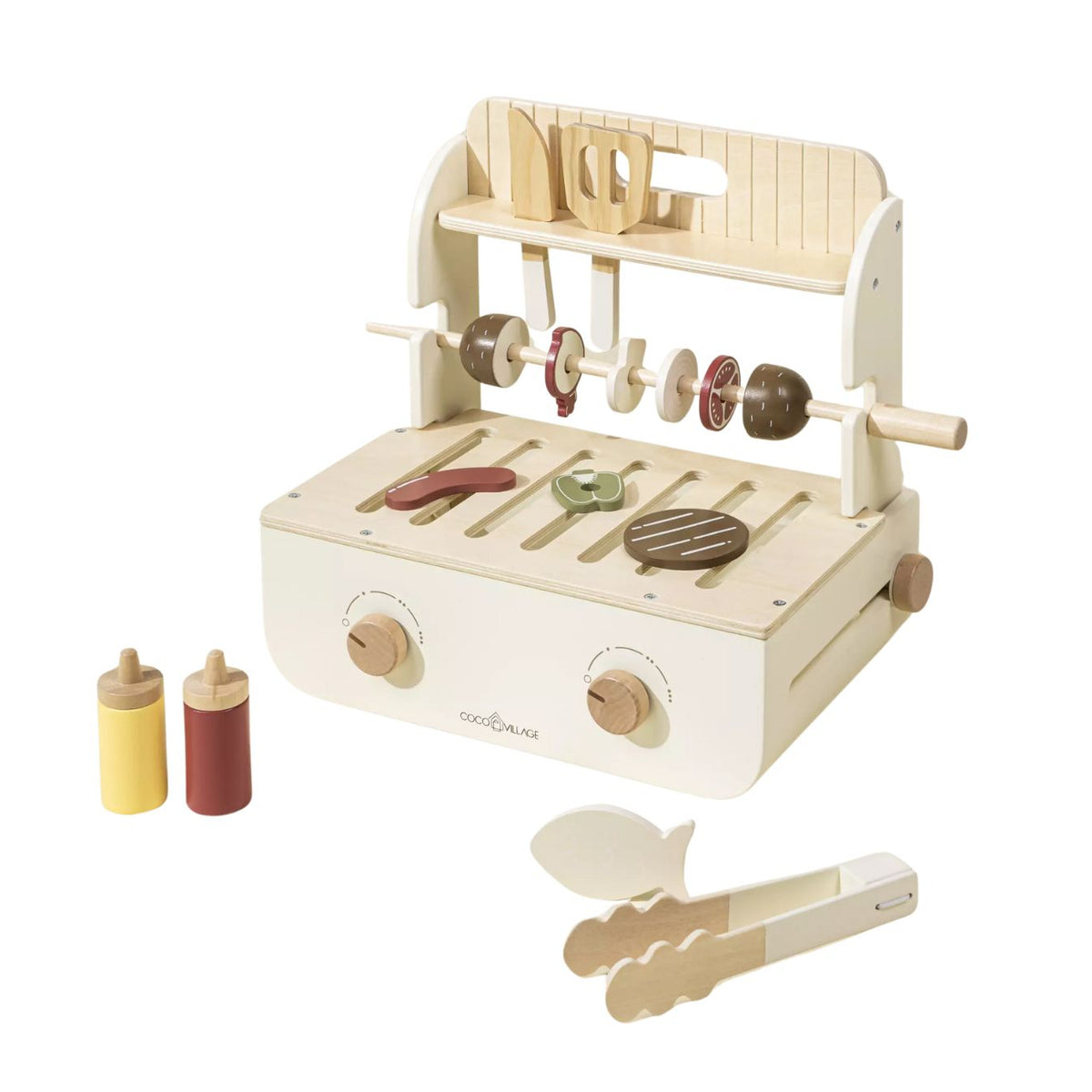 A wooden toy grill set with a cream-colored grill base, cooking rods with pretend food pieces, two small bottle-shaped condiment containers, and utensils including tongs and spatulas, photographed on a clean white background.