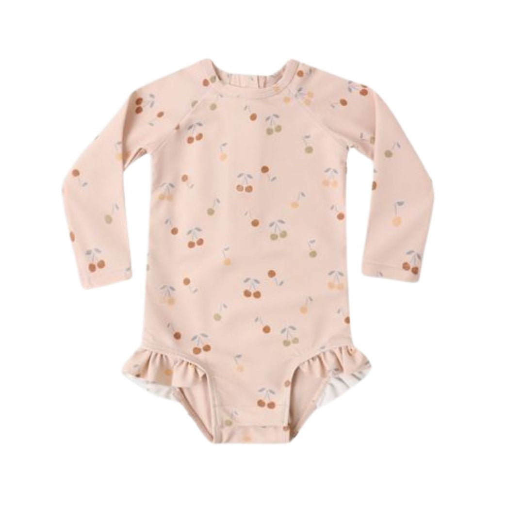 A baby long-sleeve bodysuit in a soft blush pink color, decorated with a small cherry print in brown, orange, and green, featuring a ruffled hem.